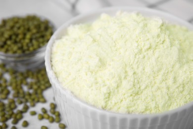 Photo of Mung bean flour in bowl and seeds on white table, closeup