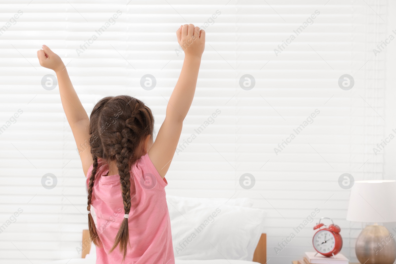 Photo of Cute little girl stretching in cosy bedroom, back view
