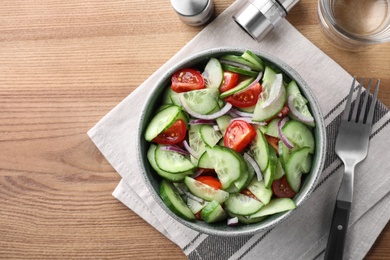 Bowl of tasty cucumber tomato salad served on wooden table, flat lay. Space for text