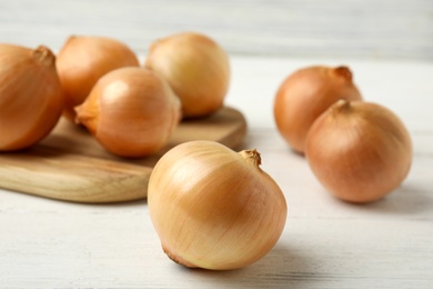 Photo of Ripe onions on white wooden table, closeup
