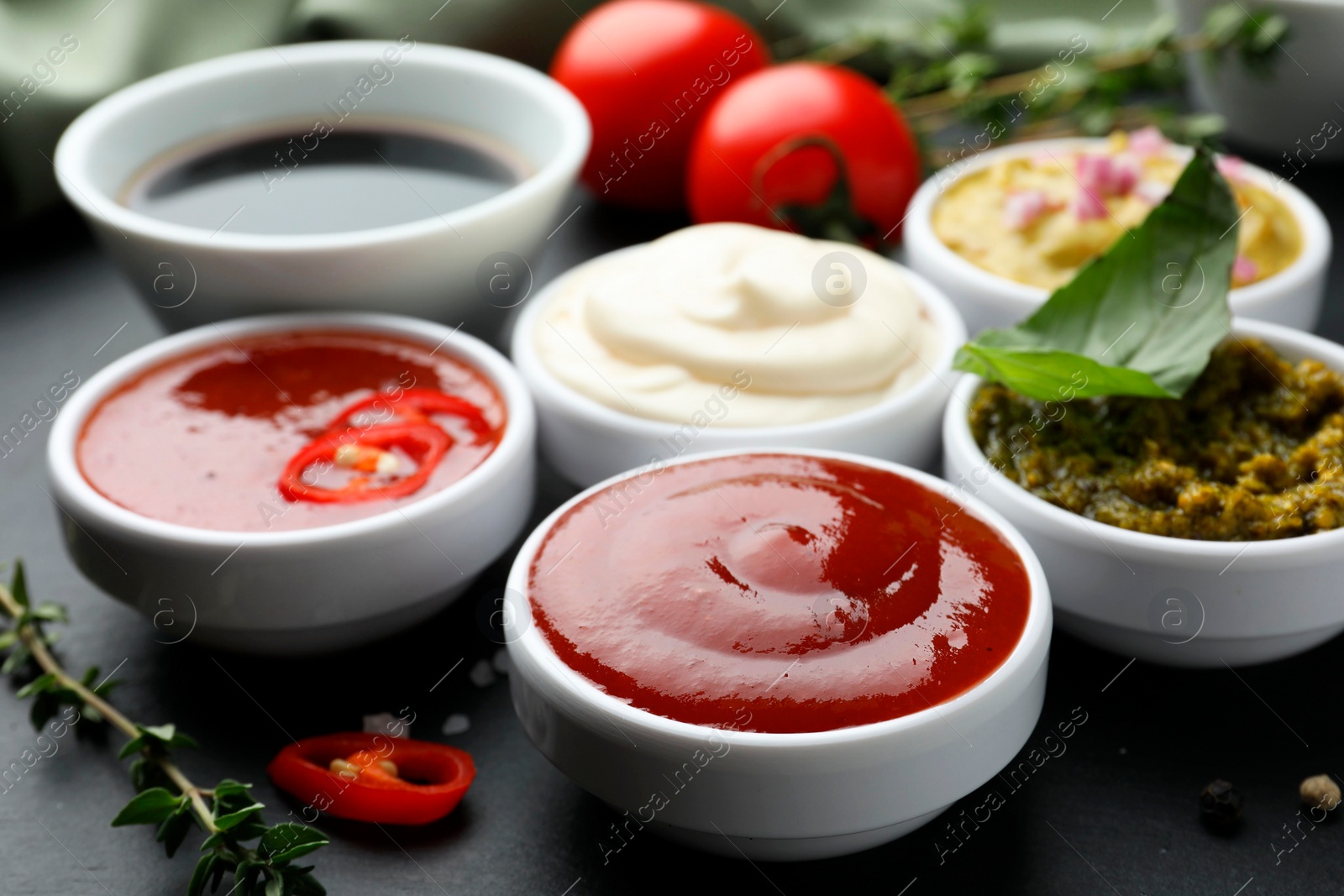 Photo of Different tasty sauces in bowls and ingredients on black table, closeup