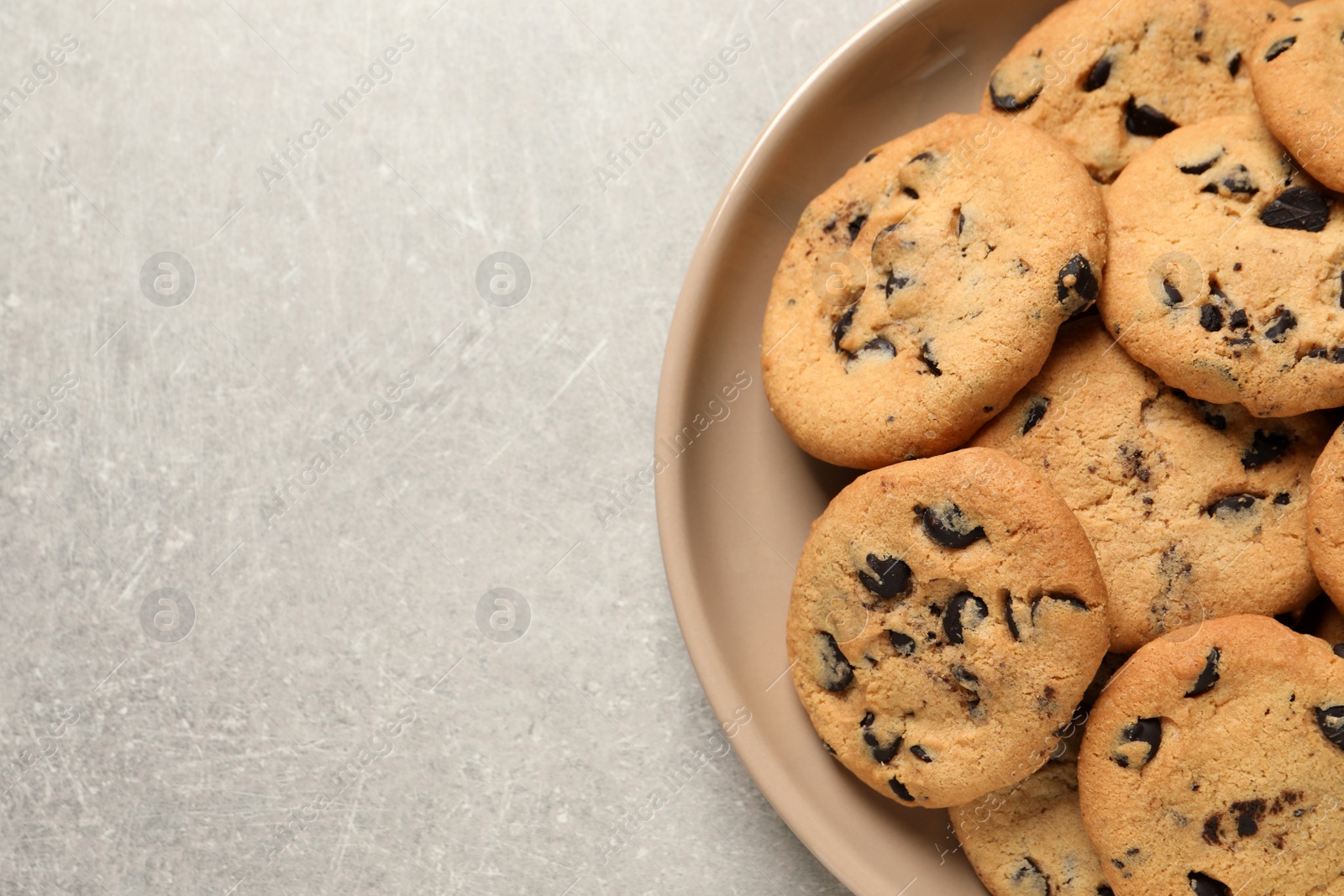 Photo of Plate with delicious chocolate chip cookies on grey table, top view. Space for text