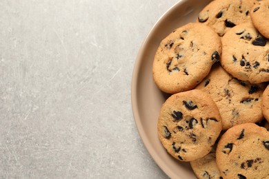 Photo of Plate with delicious chocolate chip cookies on grey table, top view. Space for text