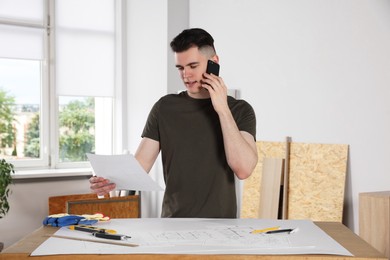 Handyman working with blueprints and talking on phone in room
