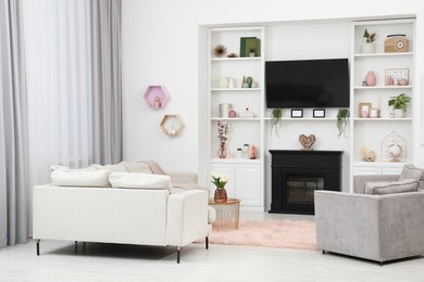 Photo of Stylish room interior with beautiful fireplace, TV set, armchairs, sofa and shelves with decor