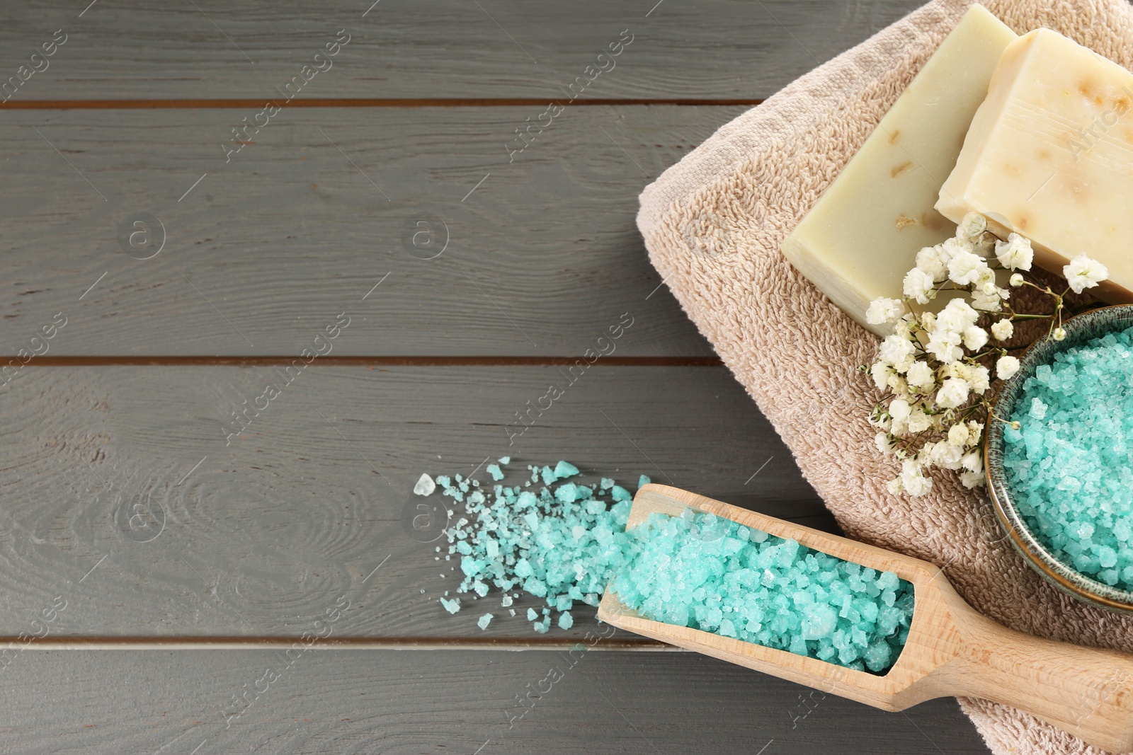 Photo of Aromatic sea salt and beautiful flowers on grey wooden table, flat lay. Space for text