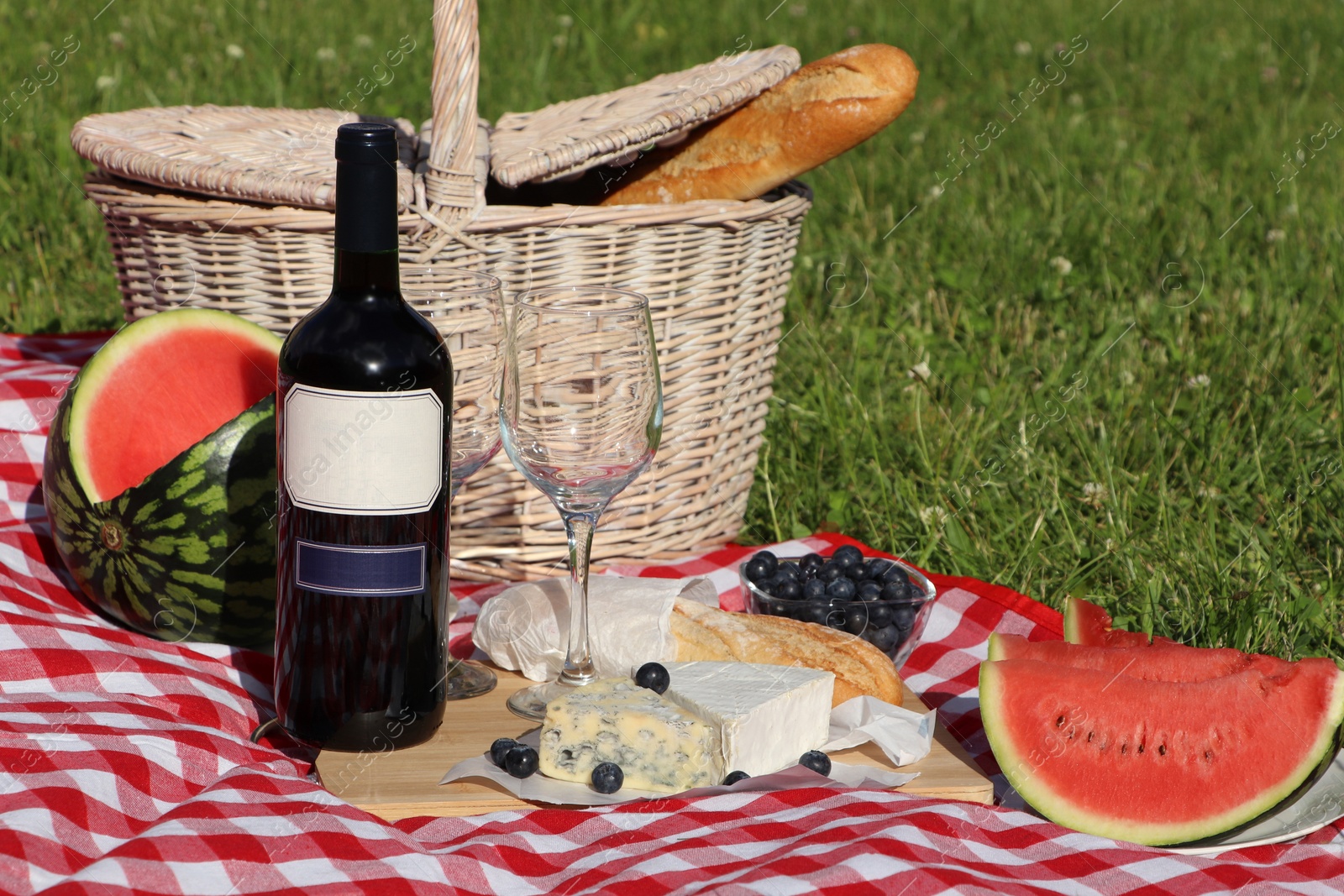 Photo of Picnic blanket with delicious food and wine outdoors on summer day