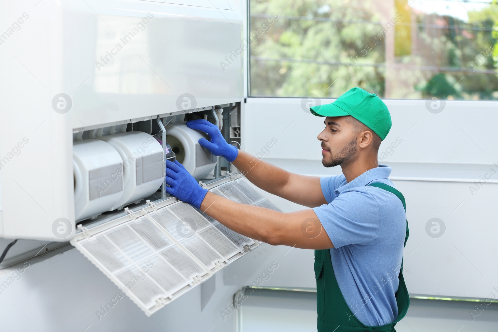 Photo of Professional technician maintaining modern air conditioner indoors