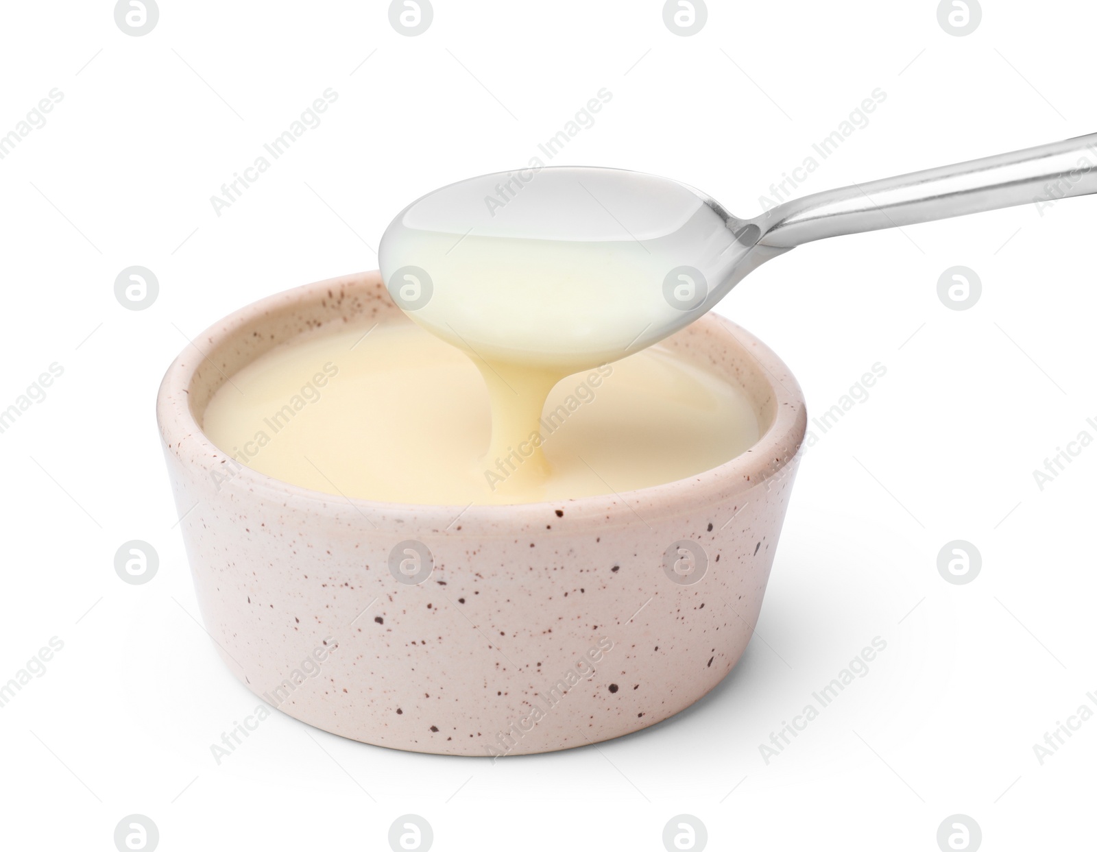 Photo of Condensed milk flowing down from spoon into bowl isolated on white