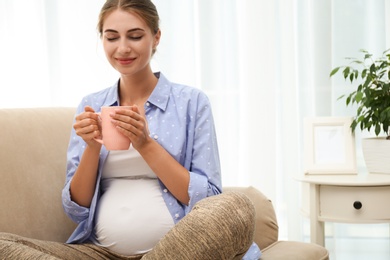 Happy pregnant woman drinking tea at home