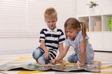 Photo of Little children playing with set of wooden road signs and toy cars indoors