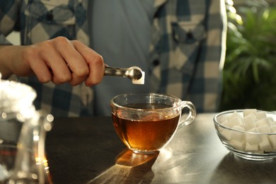 Photo of Woman adding sugar cube into cup of tea at dark table, closeup