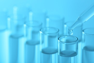 Laboratory analysis. Dripping liquid from pipette into glass test tube on light blue background, closeup