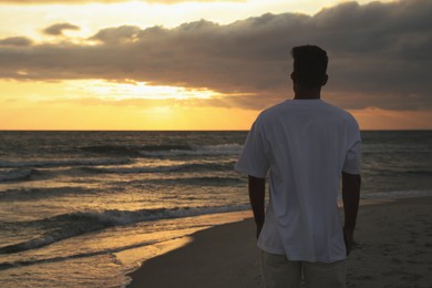 Man on sandy beach during sunset, back view