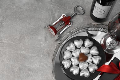 Photo of Bottle, glass of red wine, heart shaped chocolate candies, corkscrew and gift box on light grey textured table, above view. Space for text