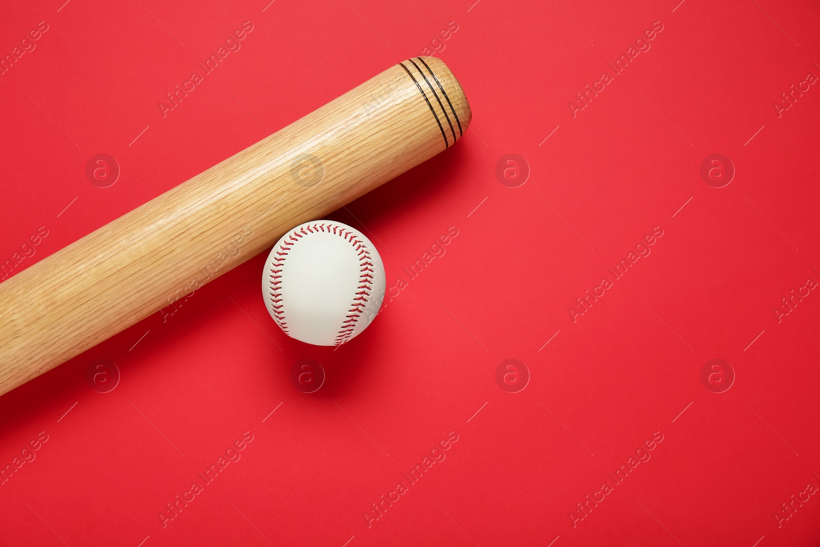 Photo of Wooden baseball bat and ball on red background, flat lay. Space for text