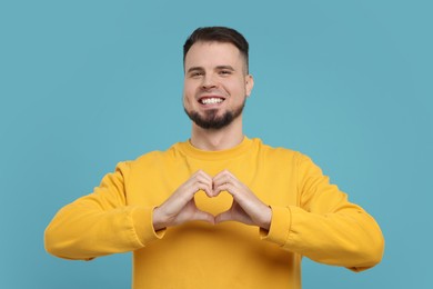 Man showing heart gesture with hands on light blue background