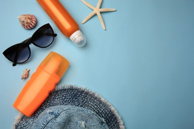 Flat lay composition with bottles of sunscreen on light blue background. Space for text