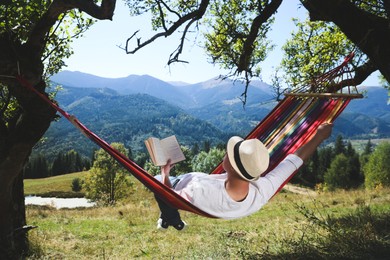 Man reading book in hammock outdoors on sunny day