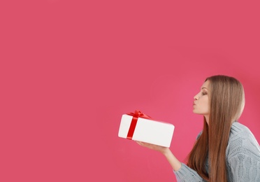 Young woman with Christmas gift on pink background. Space for text