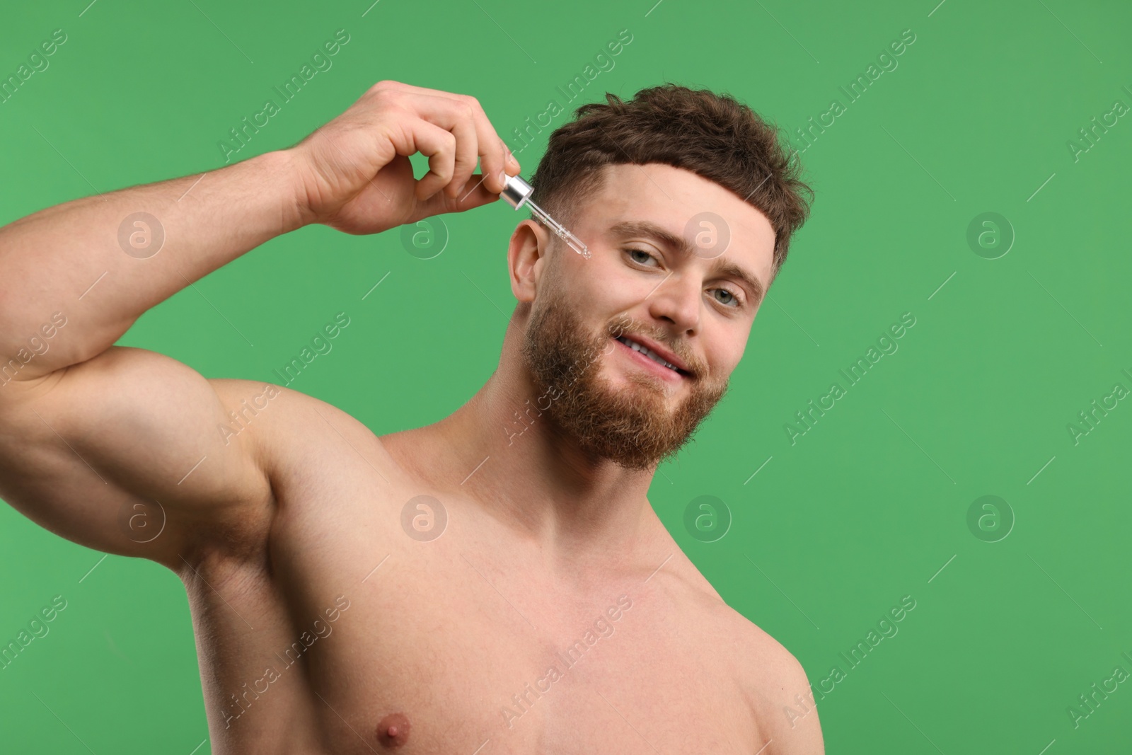 Photo of Handsome man applying serum onto his face on green background, space for text