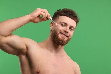 Handsome man applying serum onto his face on green background, space for text