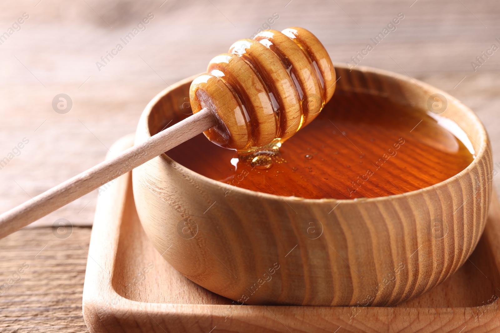 Photo of Delicious honey in bowl and dipper on wooden table, closeup