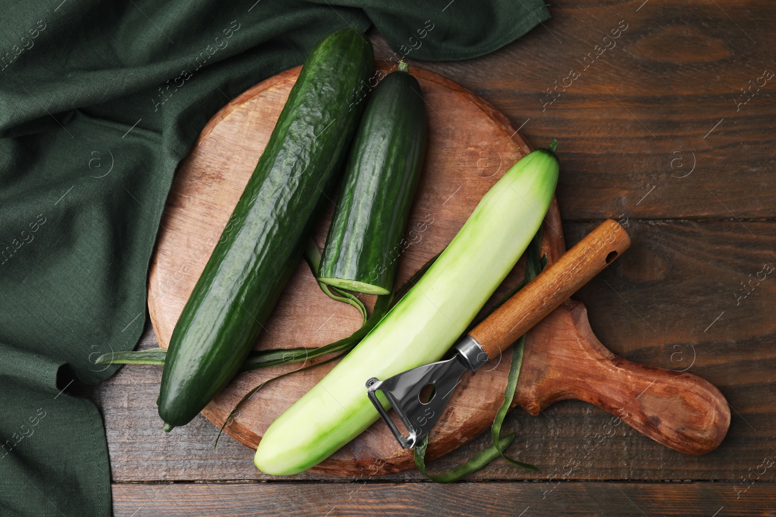 Photo of Fresh cucumbers and peeler on wooden table, top view