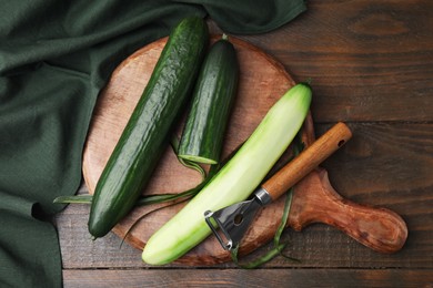 Photo of Fresh cucumbers and peeler on wooden table, top view