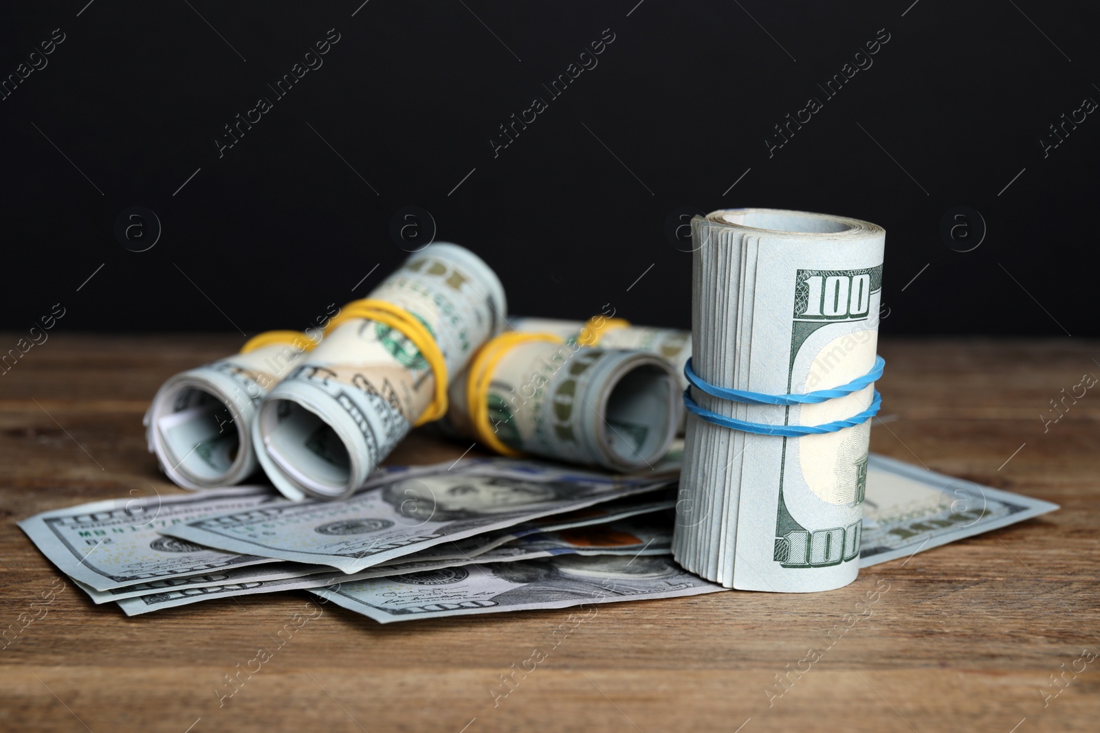 Photo of Many dollar banknotes on wooden table against black background, closeup