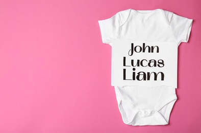 Bodysuit with different baby names on pink background, top view. Space for text