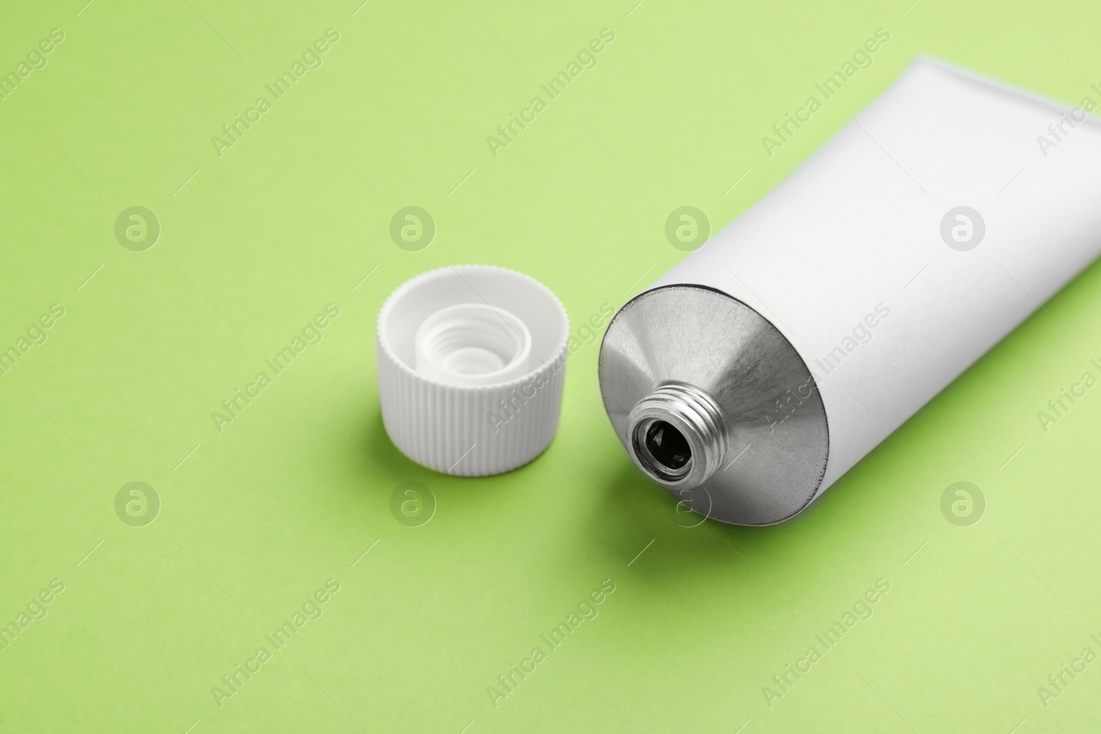 Photo of Open white tube of ointment on light green background, closeup