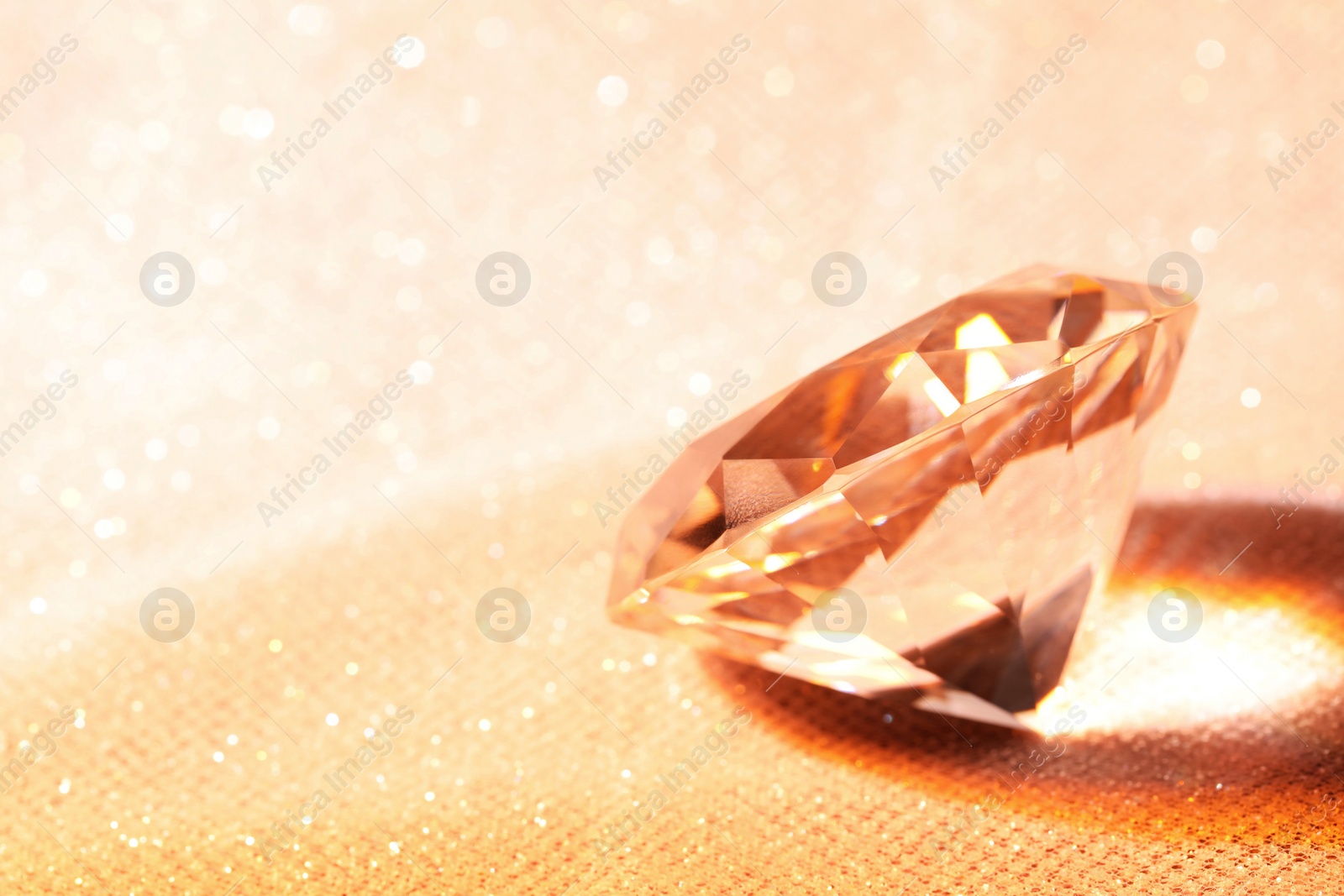 Photo of Beautiful dazzling diamond on beige glitter fabric, space for text