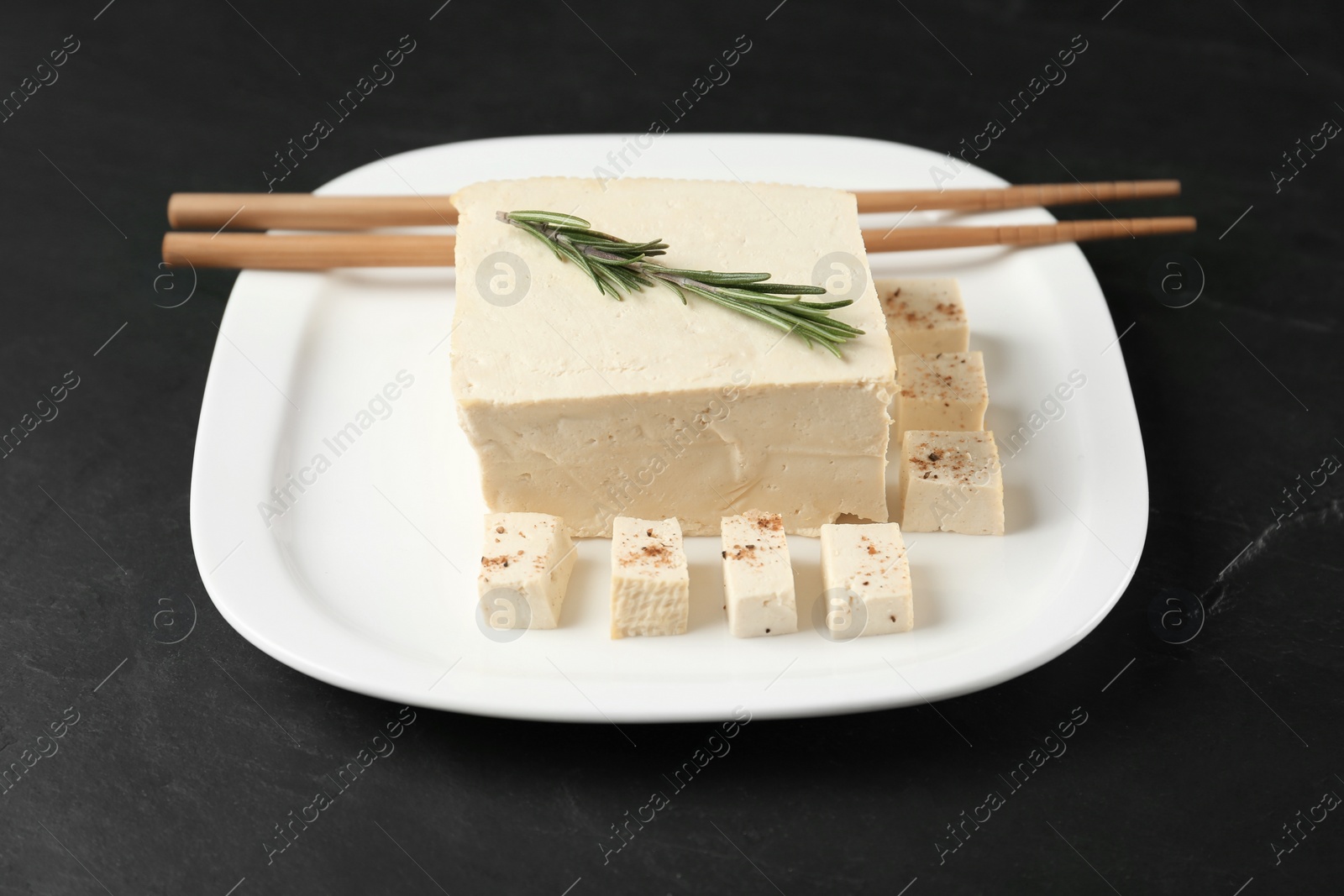 Photo of Pieces of delicious tofu with rosemary on black table. Soybean curd