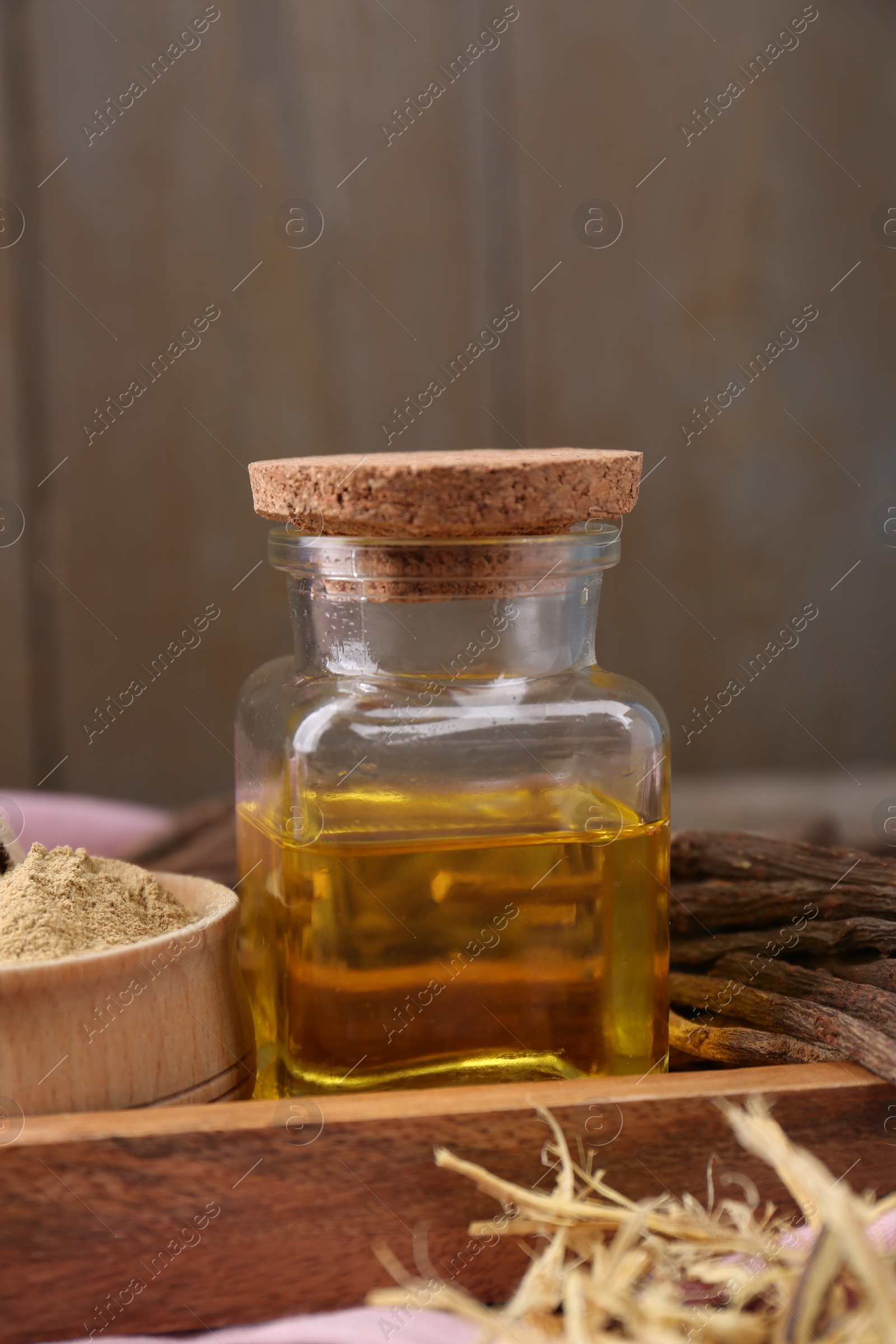 Photo of Dried sticks of licorice root, powder and essential oil on wooden board, closeup