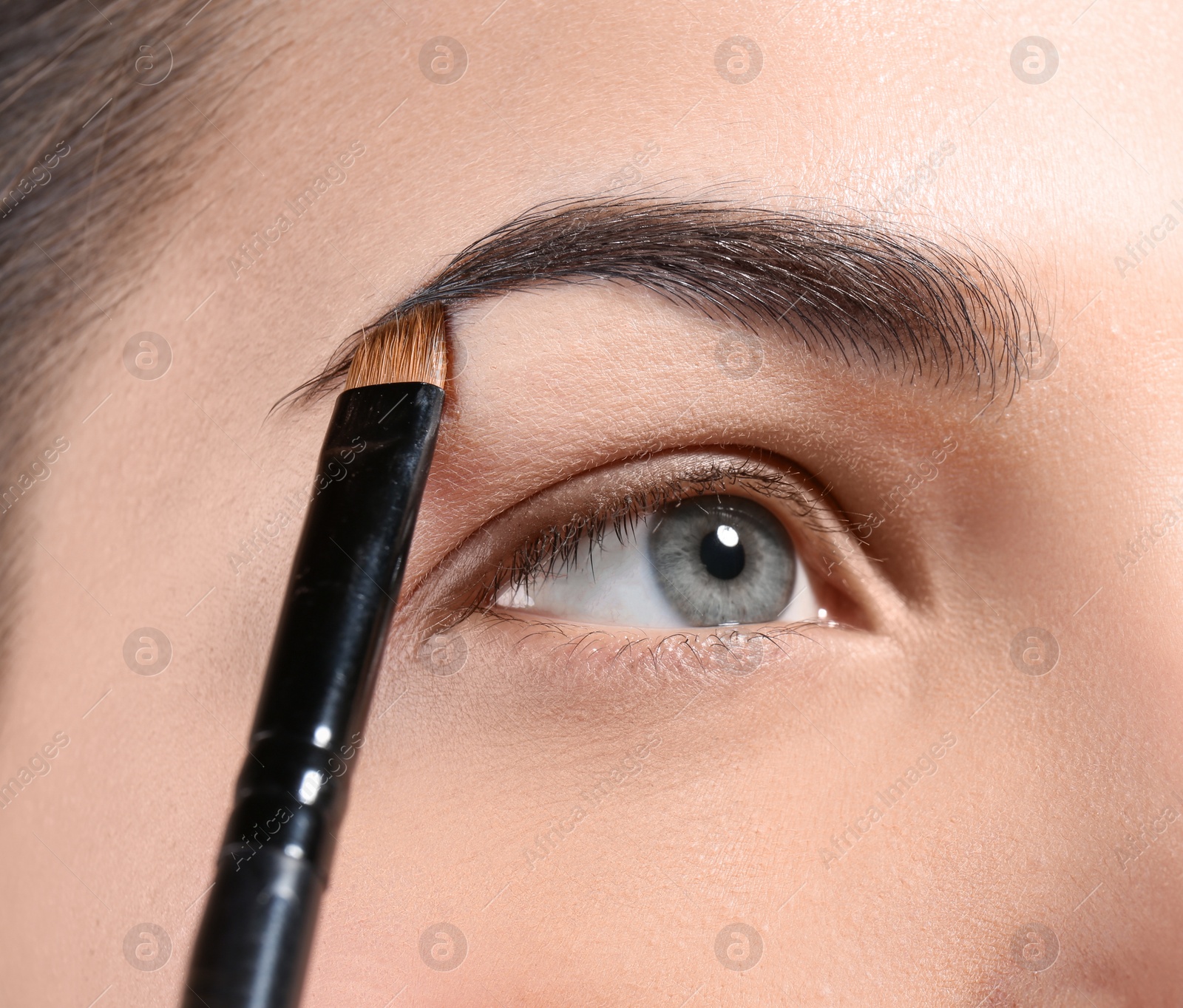 Photo of Young woman correcting eyebrow shape with brush, closeup