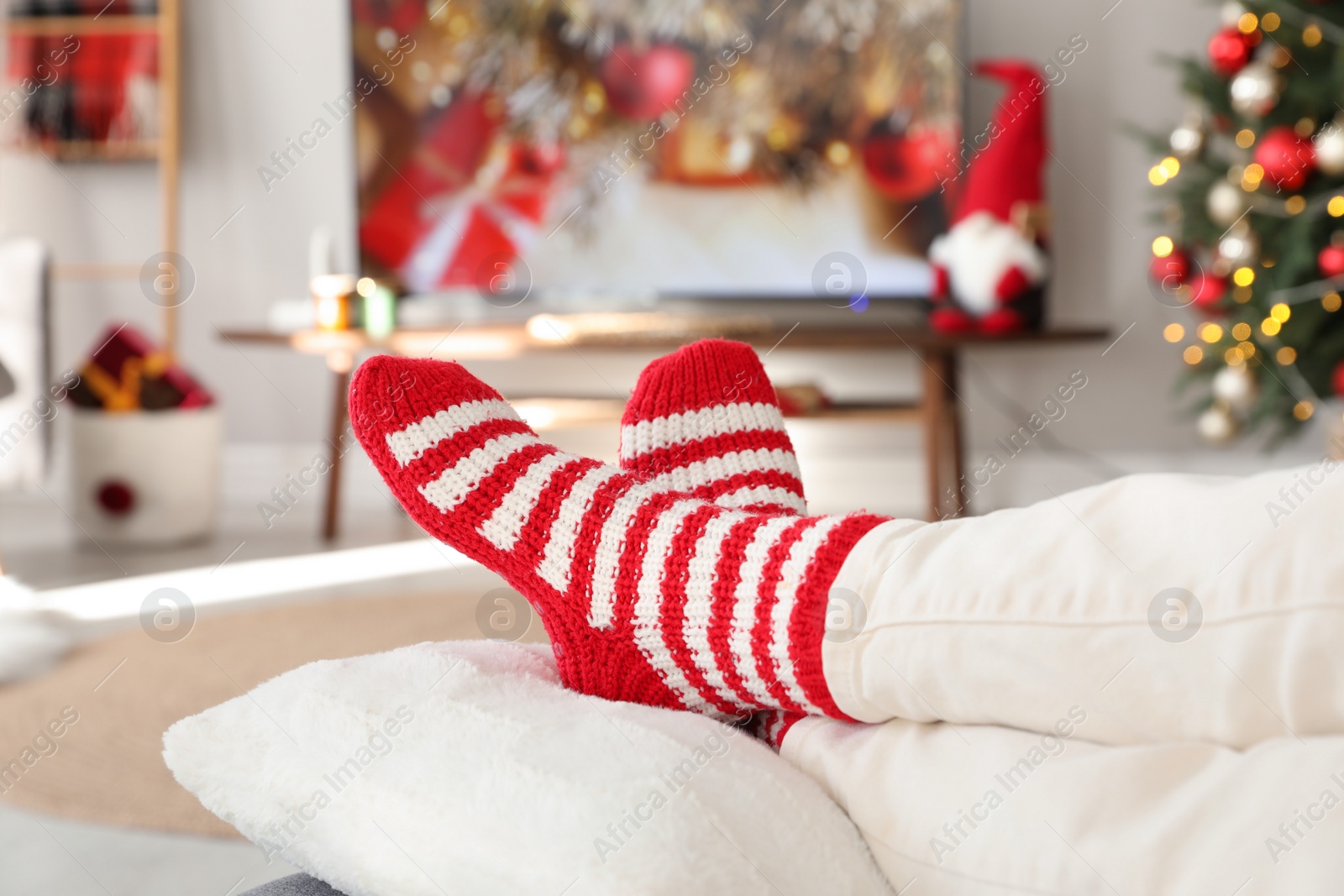 Photo of Woman in cute knitted socks watching TV at home, closeup