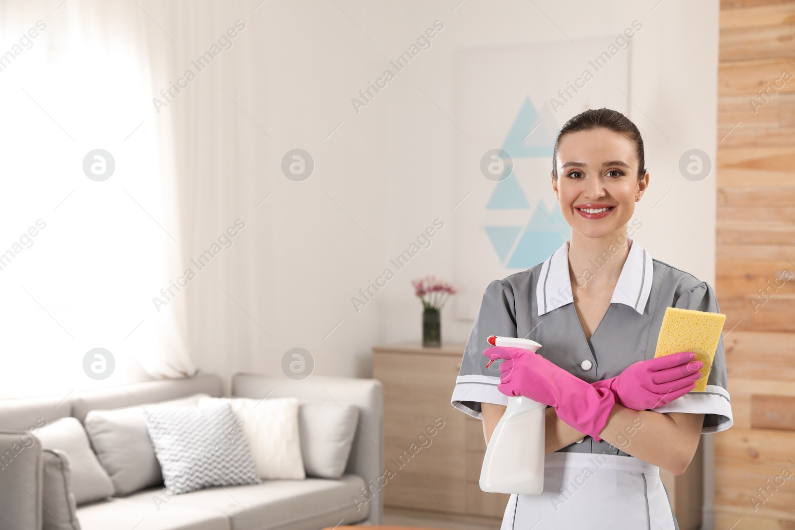 Photo of Portrait of young chambermaid with cleaning supplies in hotel room. Space for text