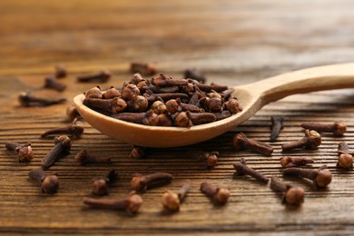 Photo of Aromatic dry cloves and spoon on wooden table, closeup