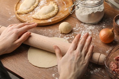Photo of Woman rolling dough for chebureki on wooden table, closeup
