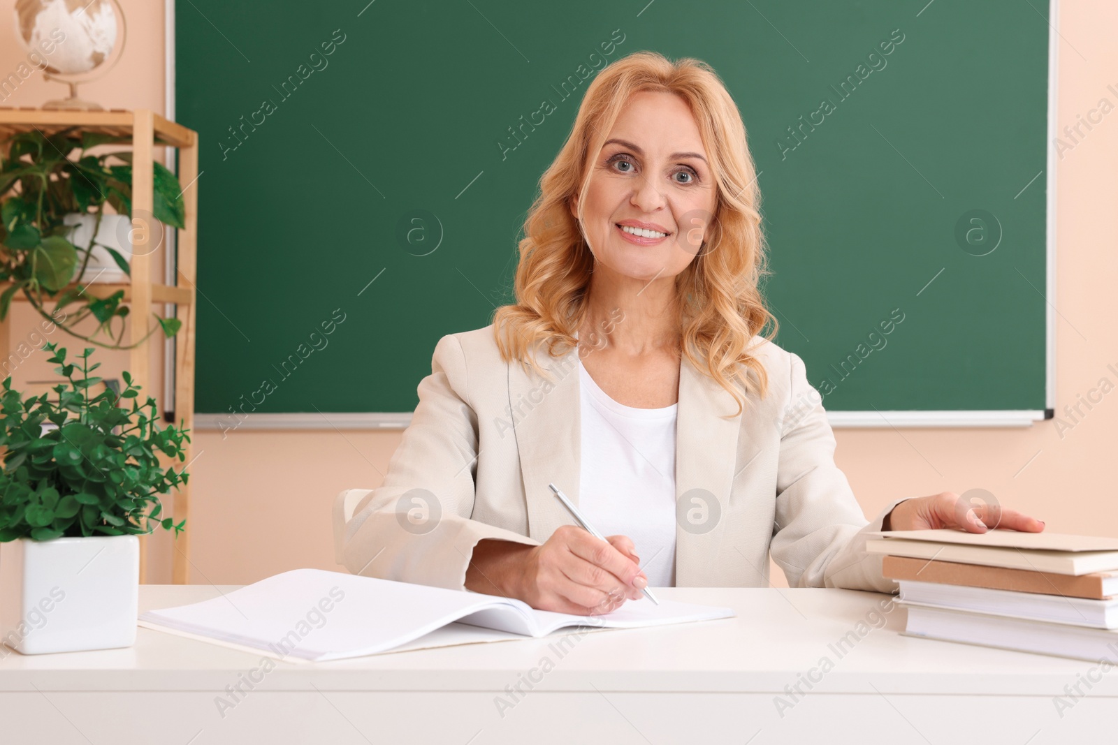 Photo of Happy professor with books sitting at desk in classroom