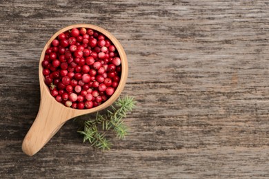 Cup with tasty ripe lingonberries and spruce twig on wooden surface, flat lay. Space for text