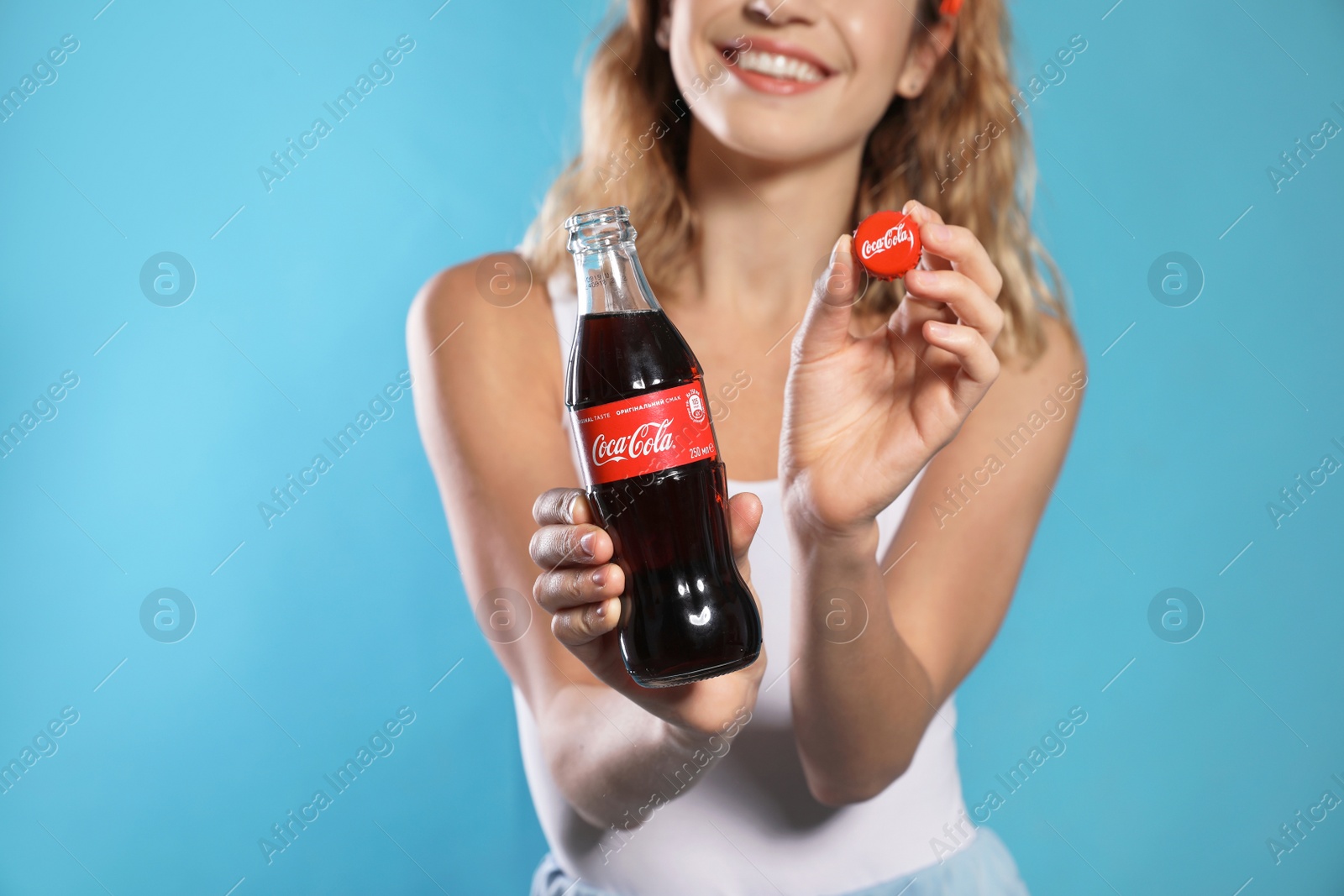 Photo of MYKOLAIV, UKRAINE - NOVEMBER 28, 2018: Young woman with bottle of Coca-Cola and cap on color background, closeup