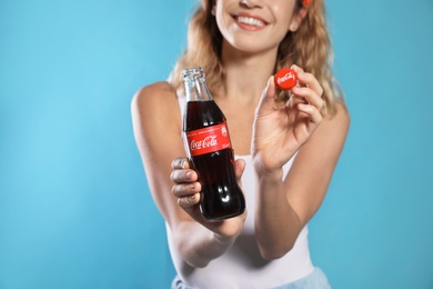 MYKOLAIV, UKRAINE - NOVEMBER 28, 2018: Young woman with bottle of Coca-Cola and cap on color background, closeup