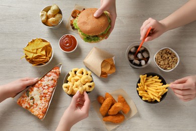 Photo of Friends eating french fries, burger and other fast food at white wooden table, top view
