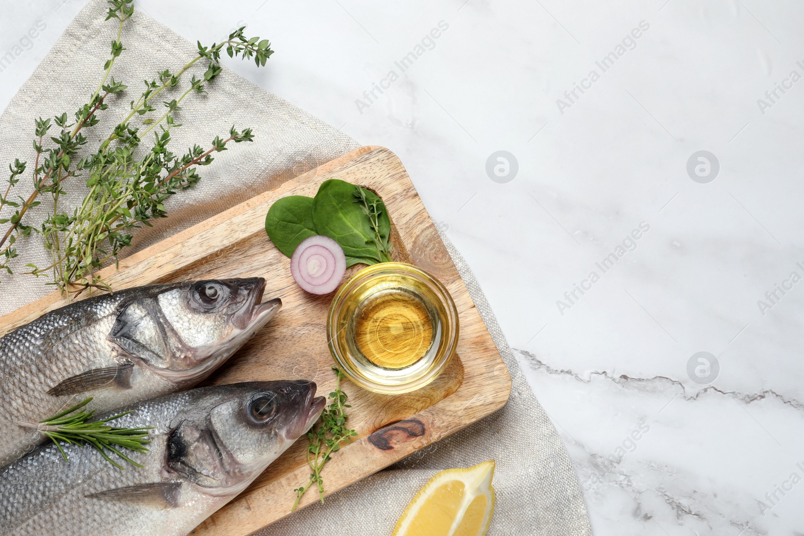 Photo of Sea bass fish and ingredients on white marble table, flat lay. Space for text