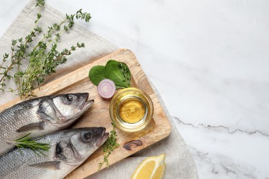 Photo of Sea bass fish and ingredients on white marble table, flat lay. Space for text