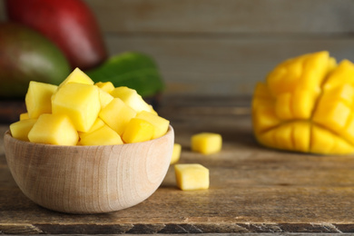 Cubes of fresh ripe mango in bowl on wooden table. Space for text