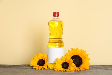 Photo of Bottle of cooking oil and sunflowers on wooden table