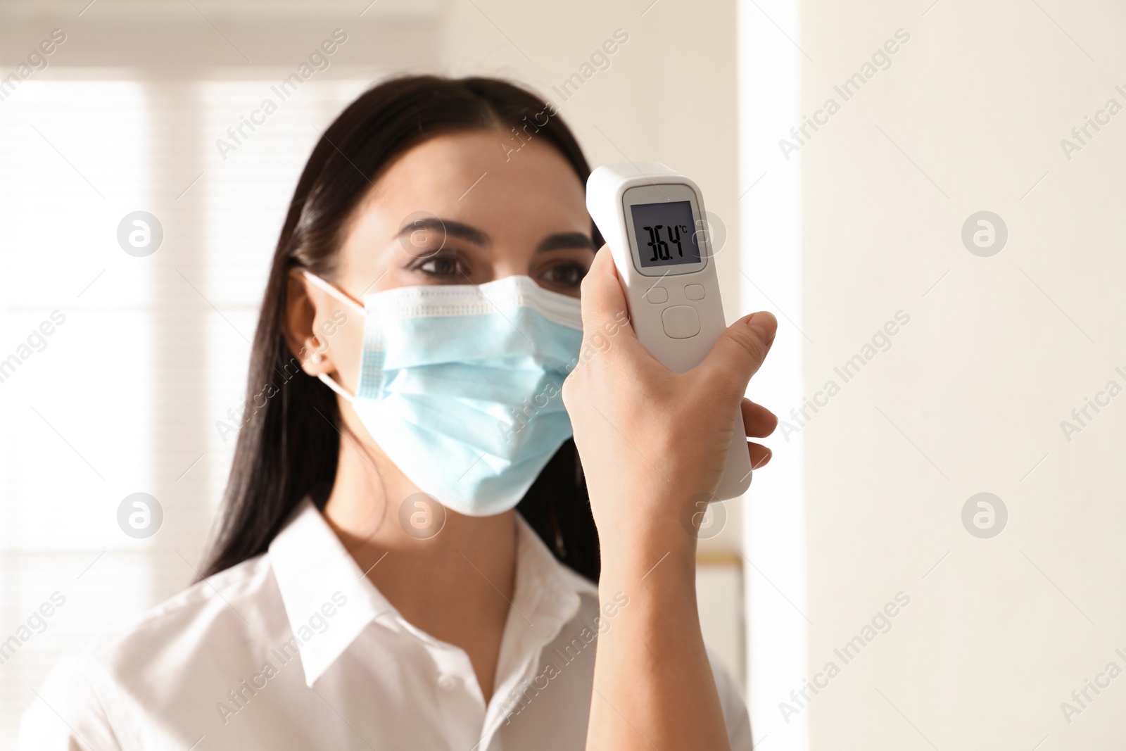 Photo of Doctor measuring woman's temperature in office, closeup. Prevent spreading of Covid-19